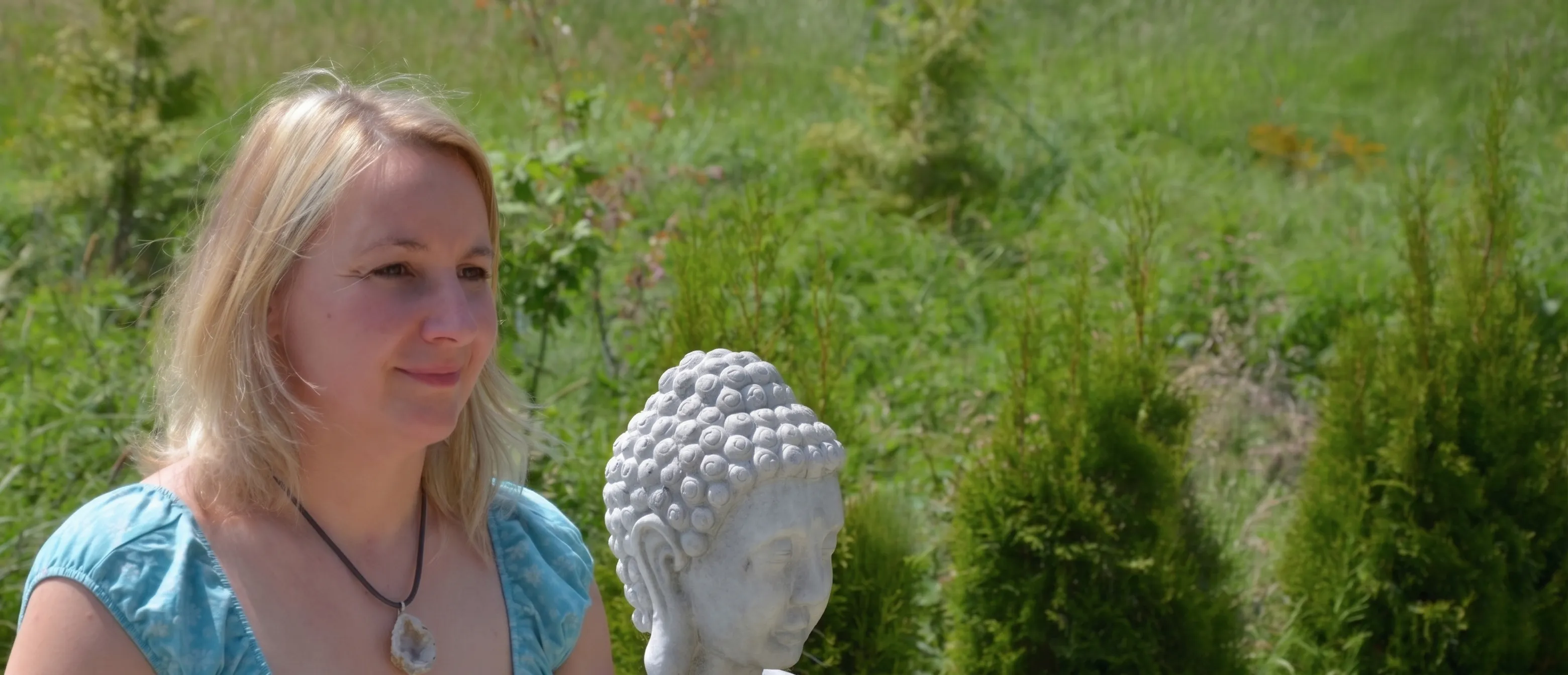 Susanne Sander, ganzheitlich-spirituelle Gesundheitsberaterin, mit Buddha- und Koi-Skulpturen in sommerlichem Garten